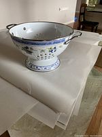 Side view of enamel colander showing floral Delft style decoration and metal handles.