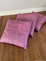 Three square pink floral accent cushions on wood floor, showing fabric detail and condition.