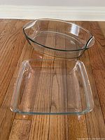 Two clear heatproof glass baking dishes on wooden floor; one rectangular 9x9 inches, one oval 9x17 inches approx. 3 quart capacity.
