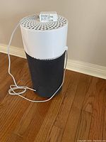 Large cylindrical air filter with black mesh and white vented top shown on wood floor with power cord on top