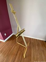 Full view of the lightweight metal artist's easel leaning against a wall showing its height and base structure