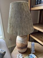 Pottery style table lamp showing full height with pleated lamp shade and ceramic base with painted abstract design.