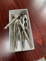 Top-down view of six metal nut and shell cracking utensils inside a small white box on wooden surface