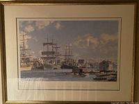 Framed large print showing several clipper ships and boats in Victoria Harbour with industrial and harbor buildings in background under a cloudy sky.