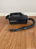 Oreck XL black portable vacuum cleaner with hose attached, shown on hardwood floor.