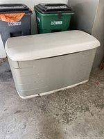 Beige plastic yard bin closed, with black and green recycling bins in the background.