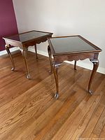 Photo showing two Queen Anne style rectangular wooden side tables with inset glass top protectors on hardwood floor.