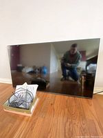 Front view of Samsung flat screen TV leaning against wall on hardwood floor, reflecting photographer