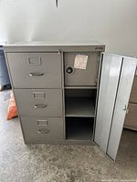 Metal filing cabinet with three closed drawers on left, open safe door on right showing interior shelves and combination lock dial.