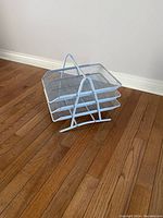 Photo of the tri-level desk tray organizer placed on a wooden floor against a white baseboard and wall.