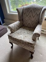 Full view of wingback chair with patterned upholstery and Queen Anne style cabriole legs, positioned in front of window
