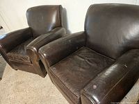 Photo showing two brown leather armchairs side by side, highlighting wear and tear including a tear on the back of one chair.
