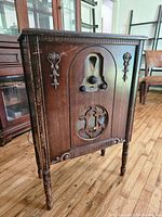 Front angled view of antique wooden radio console showing tuner dial, knobs, speaker grille, and carved details.