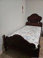 Full view of the twin bed showing mattress on frame, carved footboard and headboard visible.