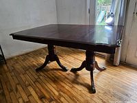 Dining room table with leaf extended showing pedestal legs and wood grain surface.