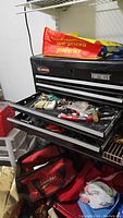 Fortress tool chest with drawers opened showing small tools, keys, hardware, and red Milwaukee tool bags underneath