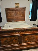Full view of king size wooden bed frame made of decorative burled wood panels with carved floral motifs on the footboard and matching headboard.