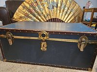 Front angled view of large black metal trunk with visible wear and missing locking parts.