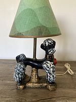 Front side view of the chalk ware poodle lamp showing the black and white poodle figure with gold collar and red tag, conical green paper shade.