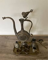 Full view of antique Arabic coffee set including largest dallah pot, six cups, smaller pitchers, small lidded container, all on metal tray