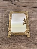 Front view of antique brass Art Nouveau vanity mirror with detailed frame and figure of a woman.