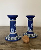Front view of blue Wedgwood jasperware candleholder pair with classical white relief decoration and walnut for size reference.