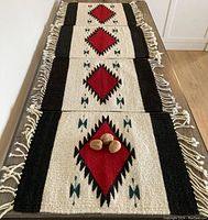 Four handmade Zapotec woven textile placemats arranged in a row showing the front side with red diamond geometric patterns, black stripes, white background, and fringed edges.