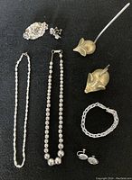 Full overview of jewelry lot showing sterling silver necklaces, sterling silver bracelet, sterling silver brooch and earrings set, and two brass mice ring holders on black background.