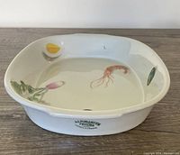 Top view of the white porcelain baking/serving dish with painted shrimp, egg, radish, and greenery designs on the interior surface.