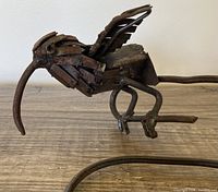 Close-up side view of one metal bird sculpture showing rusted metal strips and intricate wing and head details on a metal rod base.