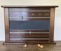 Front view of antique 1920s Honduran mahogany pool scoreboard featuring central slate chalkboard and metal sliding markers on horizontal rods above and below with gold etched scoring numbers.
