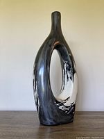Front angled view of tall, narrow Mexican pottery vase with central oval opening and black and white brushstroke finish.