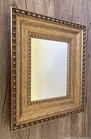 Front angled view of vintage wall mirror showing the decorative wooden frame with beaded edges and natural wood grain.