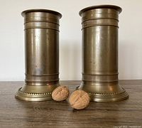 Front view of two vintage solid brass pillar candleholders placed next to each other with two walnuts in front for scale and detail.