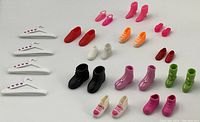 Full lot view showing various Barbie vintage shoes and plastic hangers in multiple colors and styles arranged in rows on beige surface.