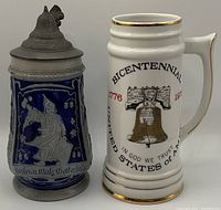 Photo of two collectible steins: a blue Bavaria stein with a pewter lid featuring a figure, and a white Bicentennial stein depicting the Liberty Bell and gold trim.