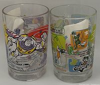 Photo of two clear glass tumblers featuring Disney characters: one with Buzz Lightyear and one with various classic Disney characters, showcasing vibrant color screen-printed designs.