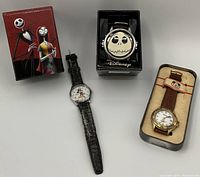 Three Disney-themed watches displayed with their original boxes and containers on a grey surface. Two feature Nightmare Before Christmas characters, one features Mickey Mouse.