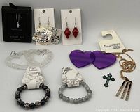 Mixed jewelry lot on white background showing necklaces, bracelets, and earrings, various styles including heart-shaped earrings, skull bead bracelet, red and purple earrings, and pendants.