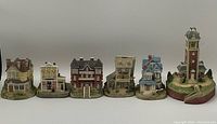 Photo showing six Liberty Falls miniature village buildings in a row including a courthouse, bakery, tavern, residential and clock tower models.