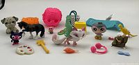 Front view of multiple Littlest Pet Shop animal figures and various plastic toy accessories arranged on a white surface