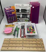 Photo of entire lot showing various new office supplies including glue sticks, dry-erase markers, rulers, pencil compass, eraser caps, Sharpie markers, and a purple folder.