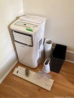 Full shot of the portable air conditioner unit with accessories laid out on floor