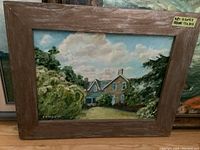 Framed oil painting showing a country house with lush greenery and partly cloudy sky. Signature C E Moule 23 visible.