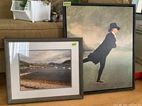 Two framed prints leaning against sofa: one is a stylized painting of a skater, the other a photographic print of sailboats on a loch.