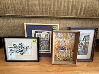 Four framed artworks displayed leaning against a couch, showing variety of styles and sizes with visible dimensions on two.