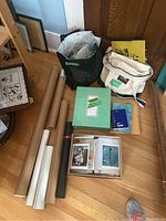 Overview of lot showing rolled posters, two bags with cards and stationery items, green box, and blue notebook