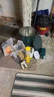 Green metal container, bird feeders, multiple bags and tins of bird food arranged on basement floor against wall