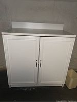 Front view of white laminate cabinet with two doors and silver handles against basement wall.