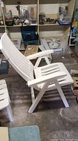 Side angle showing a white resin patio chair with slatted back and armrests.